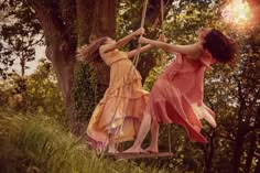 two women in dresses swinging on a swing