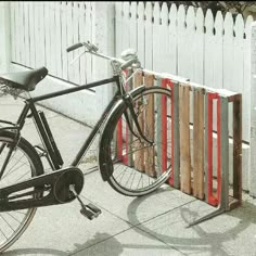 a bike parked next to a fence on the side of the street with it's shadow