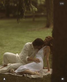 a man and woman are laying on a blanket in the grass, kissing each other