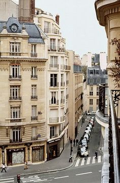 an aerial view of a city street with buildings in the background and people walking on the sidewalk