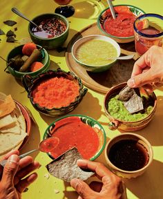 several people are eating salsa and tortillas at a table with bowls of sauces