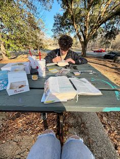 a person is sitting at a picnic table with books and papers on it while reading