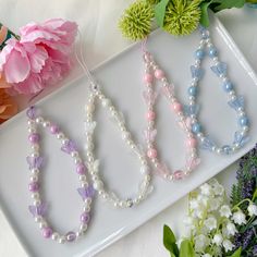 three necklaces are sitting on a tray next to some flowers and pink carnations