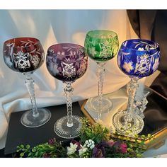 three wine goblets sitting on top of a table next to flowers and greenery