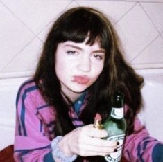 a young woman holding a beer bottle in her right hand and looking at the camera