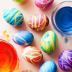 several colorful painted eggs sitting on top of a white table next to paint tubes and an orange container