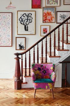 a chair sitting in front of a stair case with pictures on the wall behind it