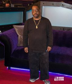 a man standing in front of a purple couch and televisions on the wall behind him