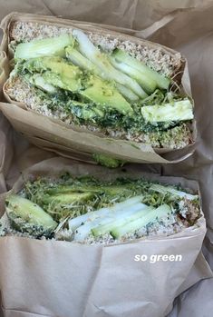 two sandwiches with broccoli and cheese in paper wrappers on top of each other