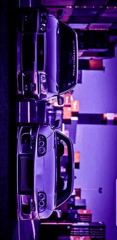 two cars are parked next to each other in a parking garage with purple hues