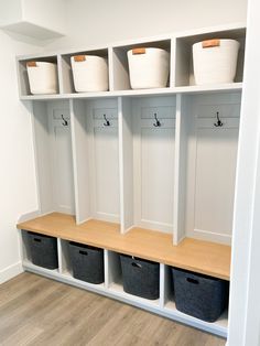 an organized mudroom with baskets and bins on the wall, along with white walls