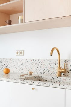 a white kitchen with gold faucet and marble counter tops, along with wooden cabinets