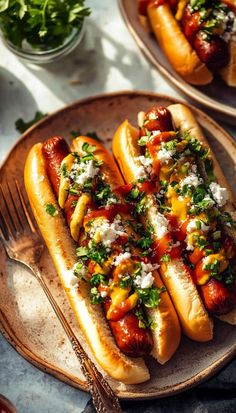 two hot dogs with toppings sit on a plate next to a fork and knife