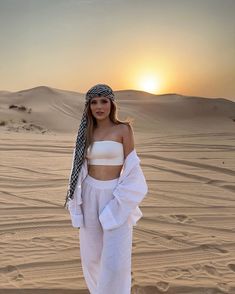 a woman standing on top of a sandy beach next to the sun in the sky