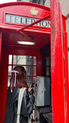 a woman standing in front of a red phone booth