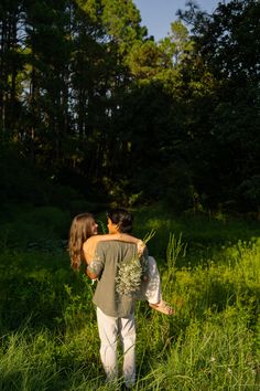 a man and woman are walking through tall grass in front of some trees with their backs to each other