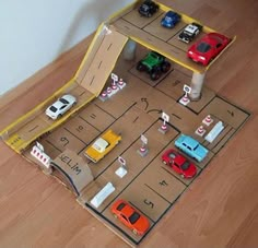 toy cars are parked on the floor in front of a parking lot with an open cardboard box