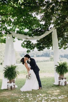 a bride and groom kissing under an arch with white draping on it at their wedding