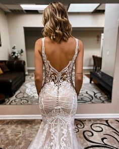 a woman in a white wedding dress looking at the back of her gown, which is open