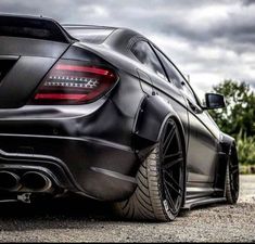 the rear end of a black car parked on gravel