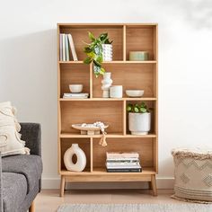 a living room with a gray couch and wooden shelves filled with books, vases and plants