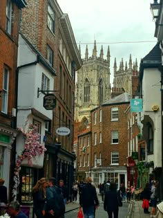 people are walking down the street in an old european city with tall buildings on either side