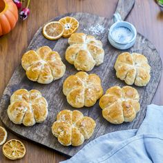 freshly baked breads on a wooden cutting board with orange slices and blue cloth next to them