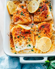 baked fish with lemons and parsley in a white casserole dish