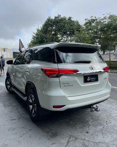 the rear end of a white suv parked in a parking lot with people walking by