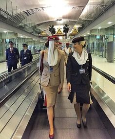 two women are walking down an escalator with luggage and people in uniform behind them