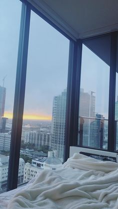 a bed sitting in front of a window next to a tall building with lots of windows