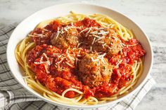 a bowl filled with spaghetti and meatballs on top of a white table cloth next to a fork