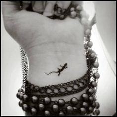 a black and white photo of a small lizard tattoo on the left wrist with beads around it