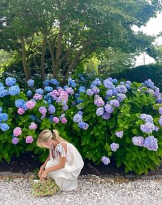 a woman kneeling down in front of blue and purple flowers