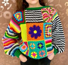 a woman wearing a multicolored sweater with flowers on the front and sides, standing in front of a floral background