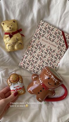 a person holding a coffee mug next to two christmas decorations and a book on a bed