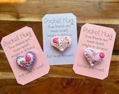 three heart shaped brooches are displayed on pink tags with white and red flowers