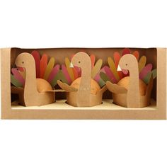 three cardboard turkeys in a box on a shelf with other paper decorations behind them