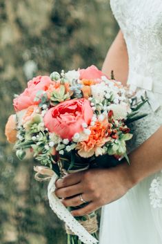 a woman holding a bouquet of flowers in her hands and wearing a wedding dress with lace