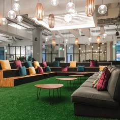 an office lounge area with green carpet, couches and tables in front of large windows