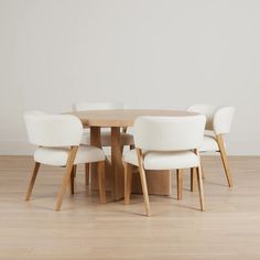 a wooden table with white chairs around it on a hard wood flooring area in front of a white wall