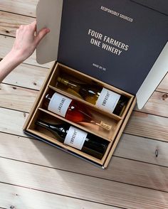 a person holding a wine box with four bottles in it on a wooden table top