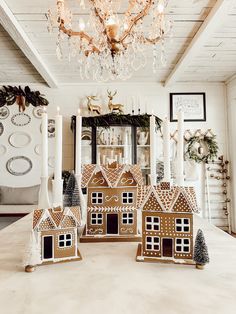 three gingerbread houses sitting on top of a table next to candles and wreaths