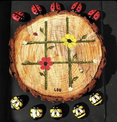 a piece of wood with ladybugs and flowers painted on it, surrounded by small black stones