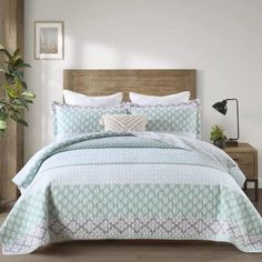 a bed in a bedroom with white walls and wooden headboard, along with a plant