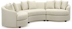 a curved sectional sofa with pillows on the top and bottom ends, in cream colored fabric