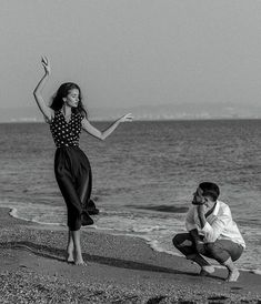 a man kneeling down next to a woman on top of a sandy beach near the ocean