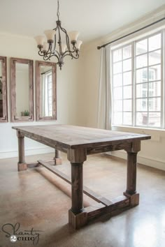 a large wooden table sitting in front of a window next to a chandelier