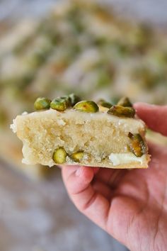 a hand holding a piece of cake with pistachios on it