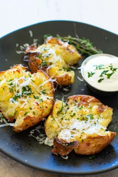 baked potatoes with parmesan cheese and herbs on a black plate next to a small bowl of ranch dressing